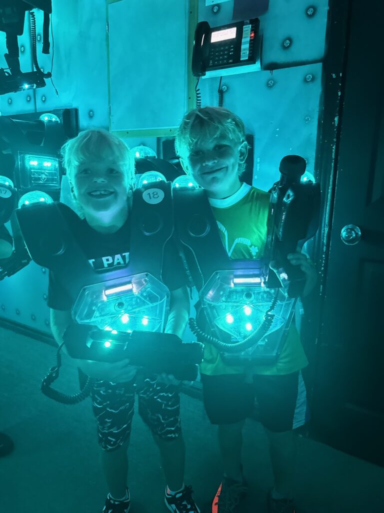 Two boys in glowing laser tag vests holding phasers and smiling